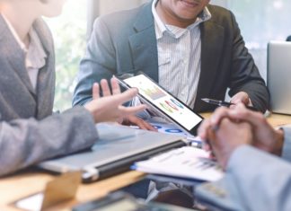 Pourquoi est-il intéressant d’investir en Bourse en temps de crise ? Personnes autour d'une tablette avec des graphiques
