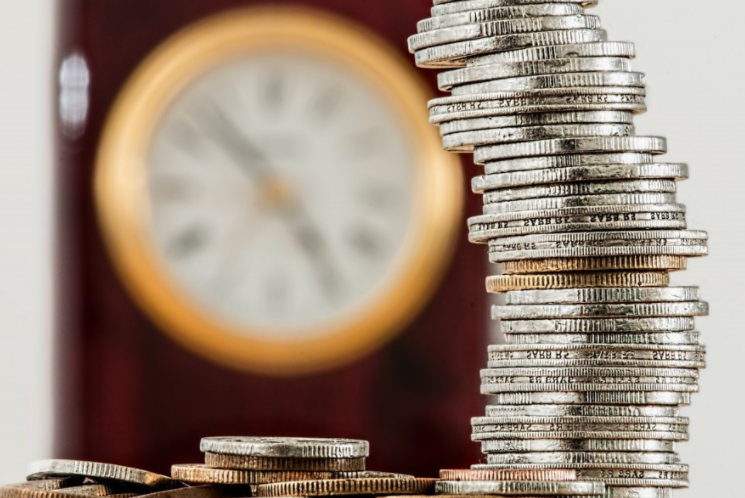 Un pile de pieces de monnaie avec une horloge en arriere plan